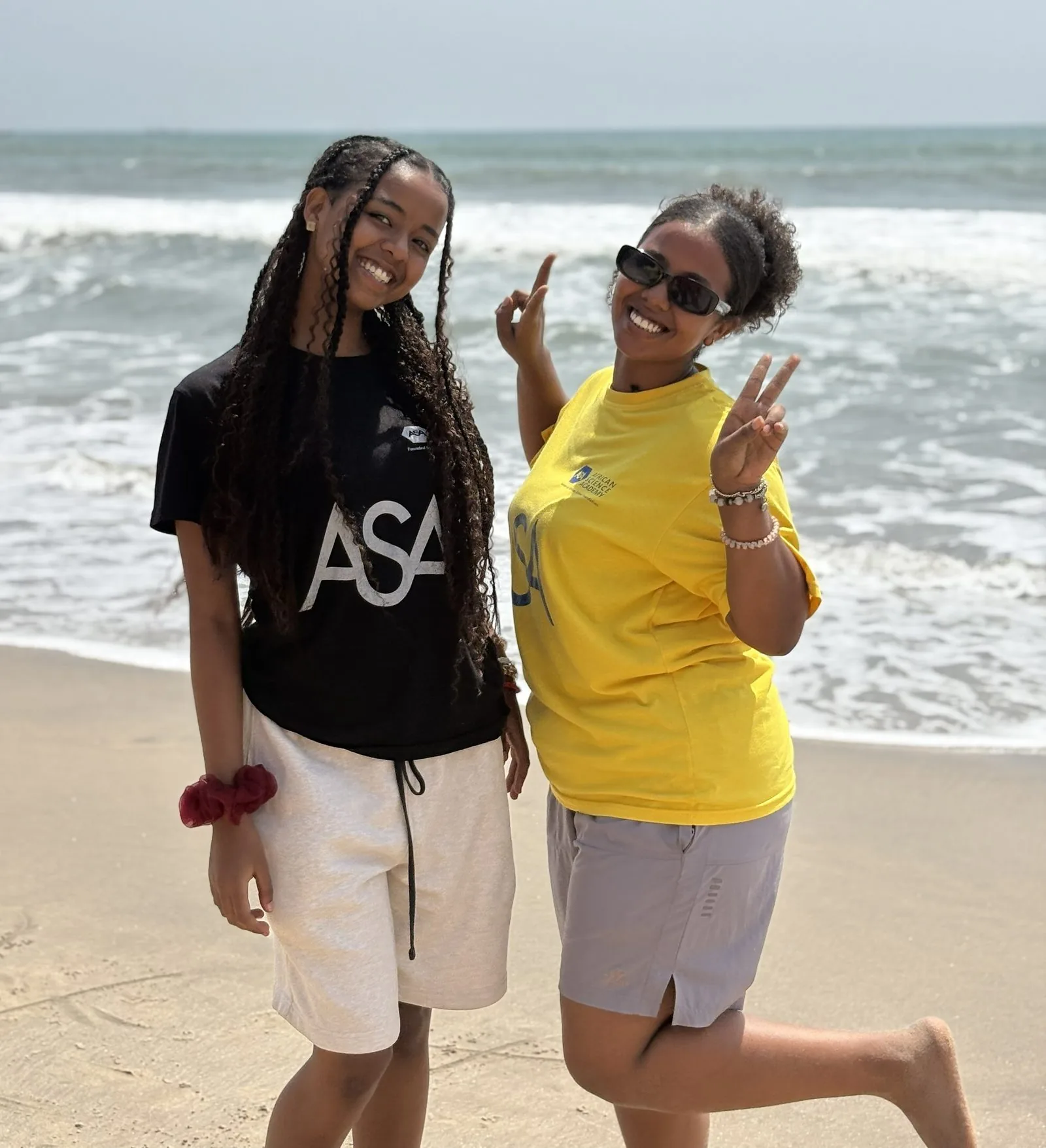 Two ASA students posing together on the beach in ASA t-shirts