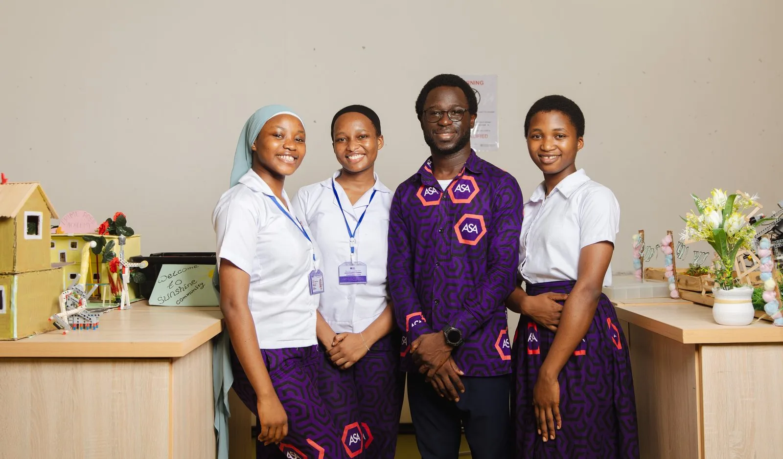 ASA graduates in traditional kente stoles posing together outside the school